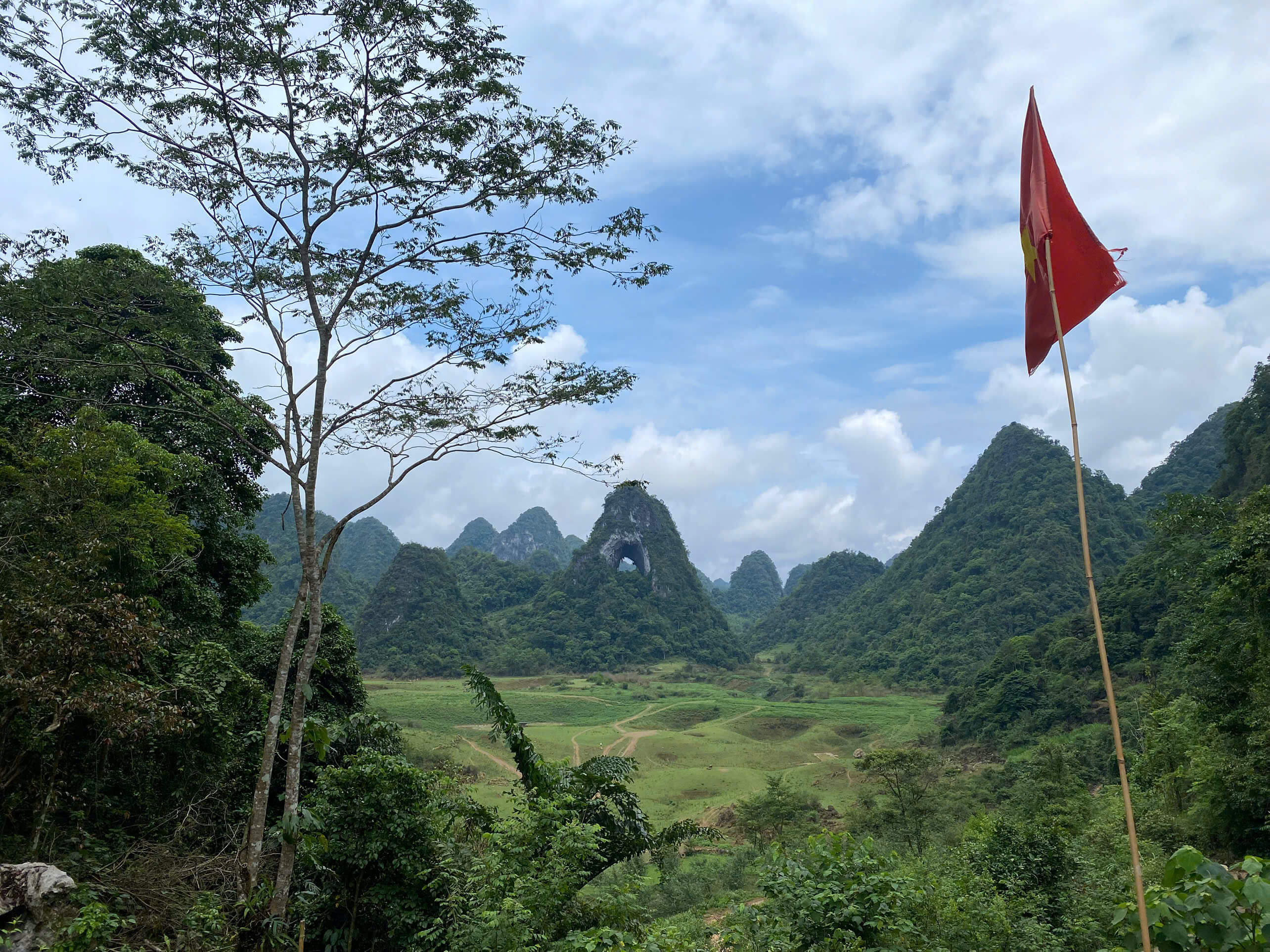 A wide view of a lush green valley featuring the unique God Eye Mountain with its distinctive hole, a major highlight of the Cao Bang motorbike loop.